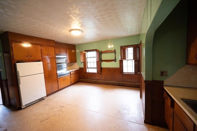 102 Margin St, Salem, MA 01970 - kitchen featuring freestanding refrigerator, brown cabinetry, a wainscoted wall, a textured ceiling, and light countertops