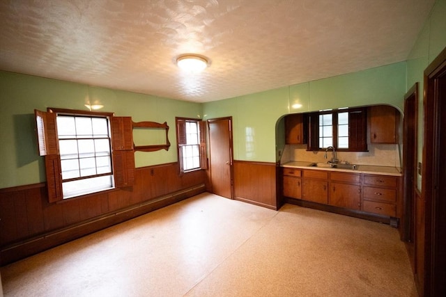 102 Margin St, Salem, MA 01970 - kitchen with wainscoting, brown cabinetry, healthy amount of natural light, a sink, and a textured ceiling