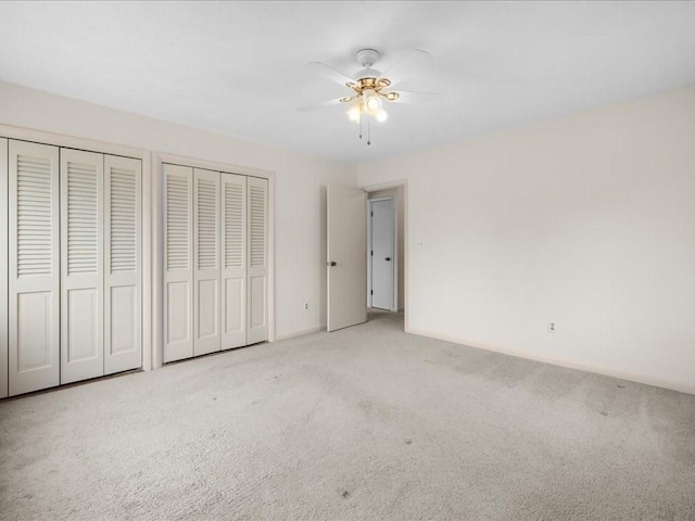 unfurnished bedroom featuring carpet, baseboards, ceiling fan, and multiple closets