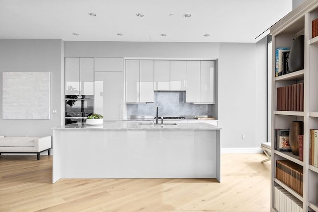 kitchen featuring white cabinetry, sink, double oven, backsplash, and light wood-type flooring