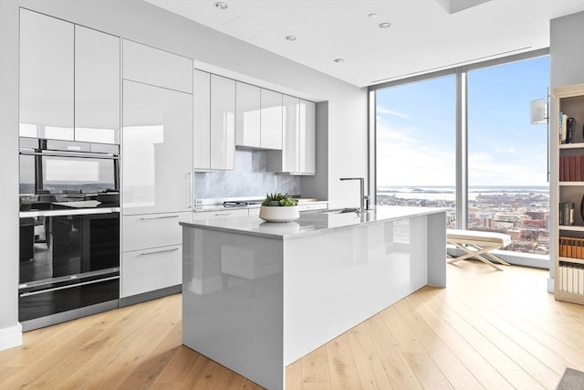 kitchen featuring white cabinets, a center island with sink, a wall of windows, and sink