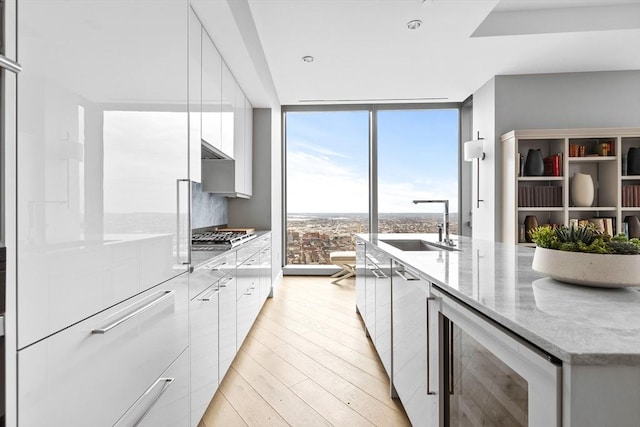 kitchen featuring white cabinetry, sink, wine cooler, light stone counters, and expansive windows