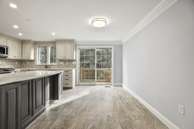 kitchen featuring sink, light stone counters, cream cabinets, decorative backsplash, and ornamental molding