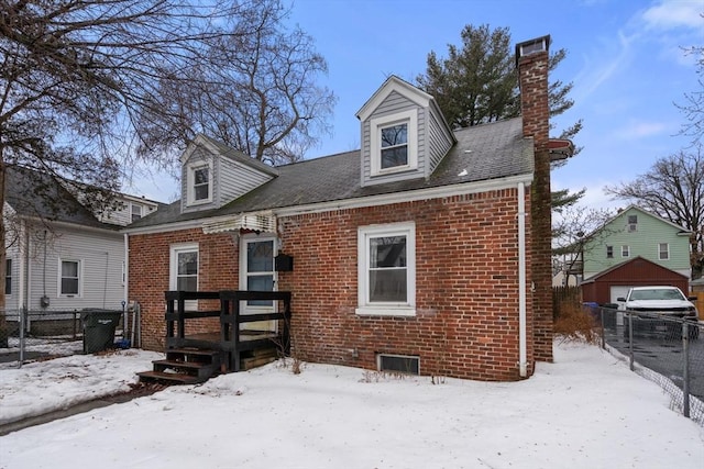 snow covered house featuring a chimney, fence, and brick siding