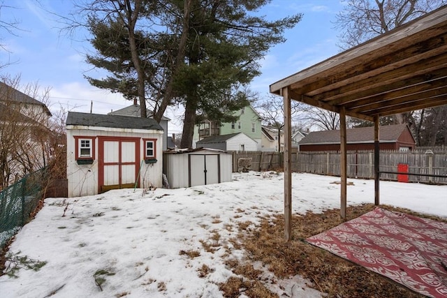 yard covered in snow featuring a fenced backyard, a storage unit, and an outdoor structure