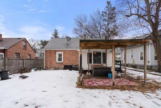 snow covered back of property featuring a fenced backyard, a fire pit, a pergola, and brick siding