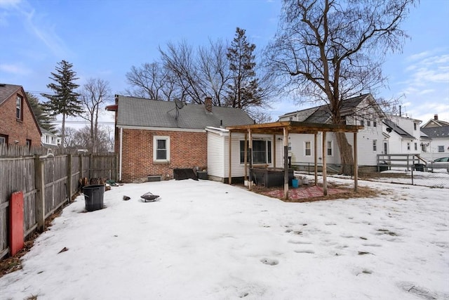 snow covered rear of property with a fenced backyard, a chimney, a pergola, and brick siding