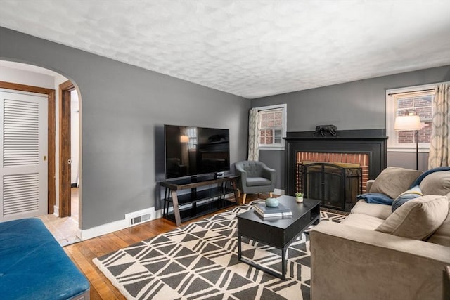 living area with baseboards, visible vents, arched walkways, wood finished floors, and a textured ceiling