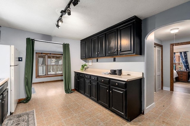 kitchen with arched walkways, light countertops, freestanding refrigerator, a textured ceiling, and dark cabinetry