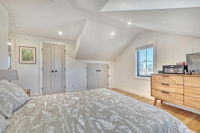 bedroom with vaulted ceiling, light wood-style floors, baseboards, and two closets