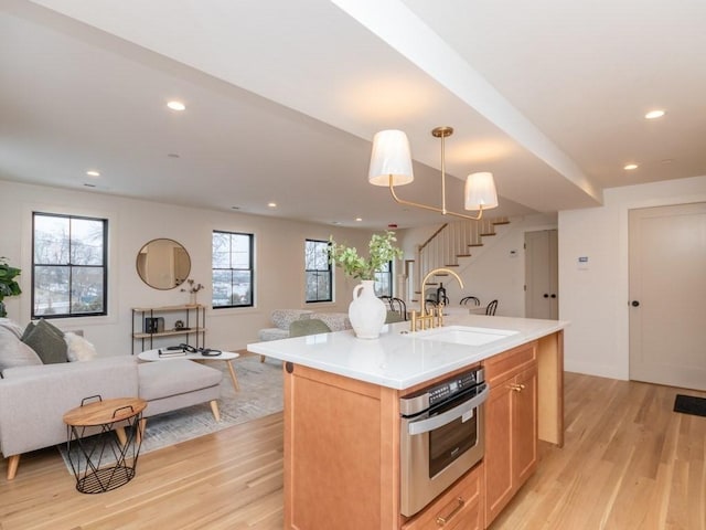 kitchen with oven, light wood-type flooring, open floor plan, and a sink