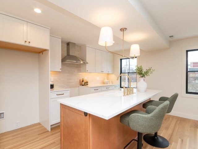 kitchen featuring a sink, decorative backsplash, white cabinets, light wood-style floors, and wall chimney range hood