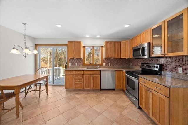 kitchen with glass insert cabinets, decorative light fixtures, a sink, stainless steel appliances, and backsplash