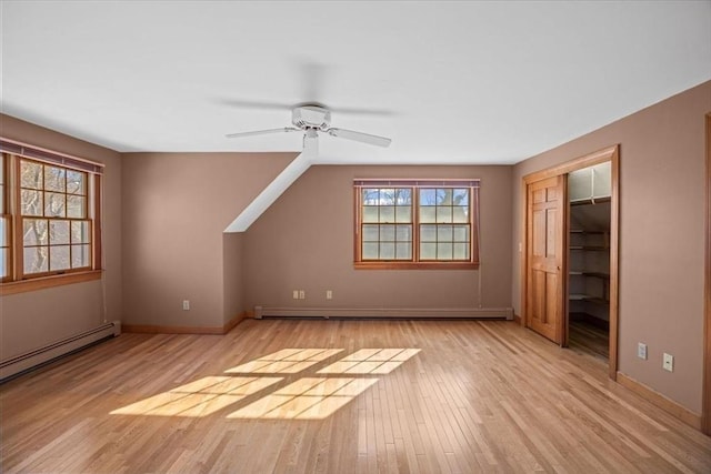 bonus room with light wood finished floors, baseboard heating, a ceiling fan, and baseboards