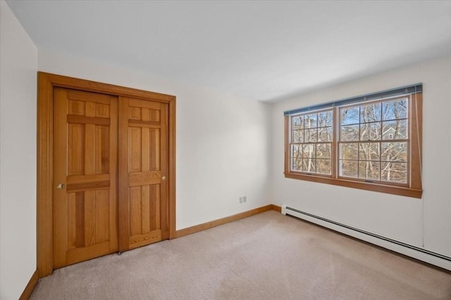 unfurnished bedroom with a baseboard heating unit, light carpet, and baseboards