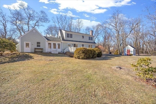 rear view of house with a chimney, a lawn, and an outbuilding