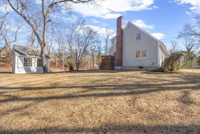 view of side of home featuring a yard, a chimney, and an outdoor structure