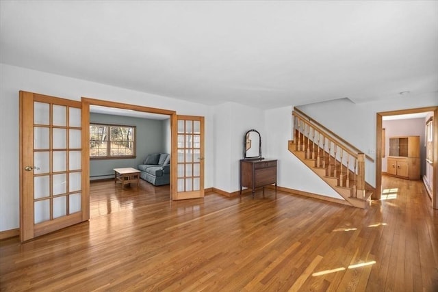 unfurnished living room featuring french doors, stairway, wood finished floors, and baseboards