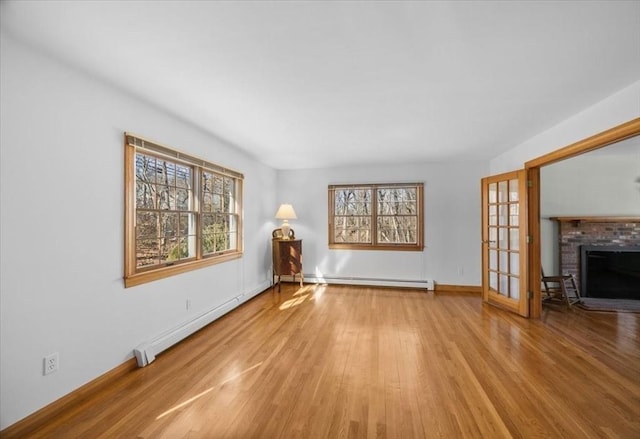 unfurnished living room featuring a brick fireplace, baseboards, baseboard heating, and wood finished floors