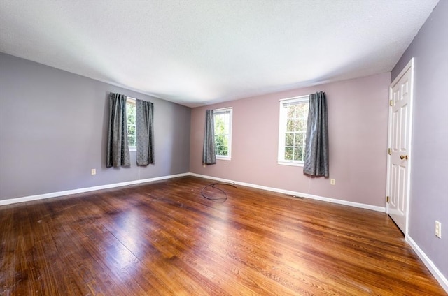 spare room with a textured ceiling, baseboards, and wood finished floors