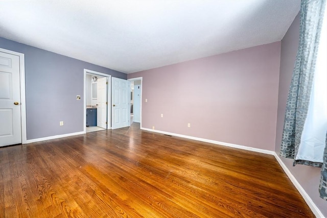 unfurnished bedroom featuring baseboards, connected bathroom, wood finished floors, and visible vents