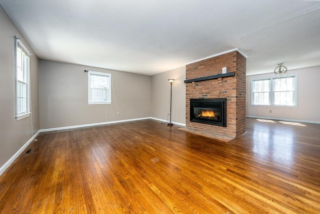 unfurnished living room with a brick fireplace, baseboards, plenty of natural light, and hardwood / wood-style flooring