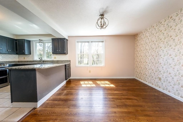 kitchen featuring wood finished floors, baseboards, wallpapered walls, range with two ovens, and tasteful backsplash