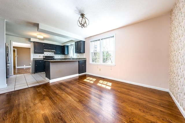 kitchen featuring a peninsula, wood finished floors, stove, under cabinet range hood, and stainless steel fridge with ice dispenser