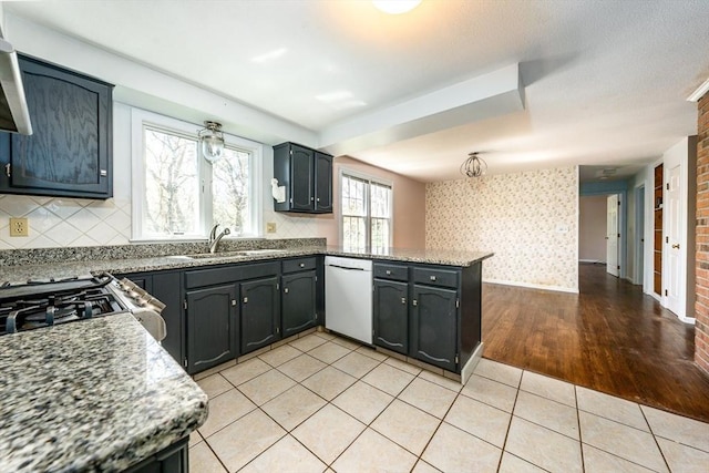 kitchen featuring stove, dishwasher, a sink, a peninsula, and light wood-style floors