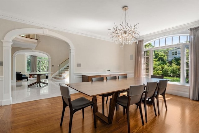69 Princeton Rd, Brookline, MA 02467 - dining space with arched walkways, ornamental molding, ornate columns, a chandelier, and light wood-style flooring