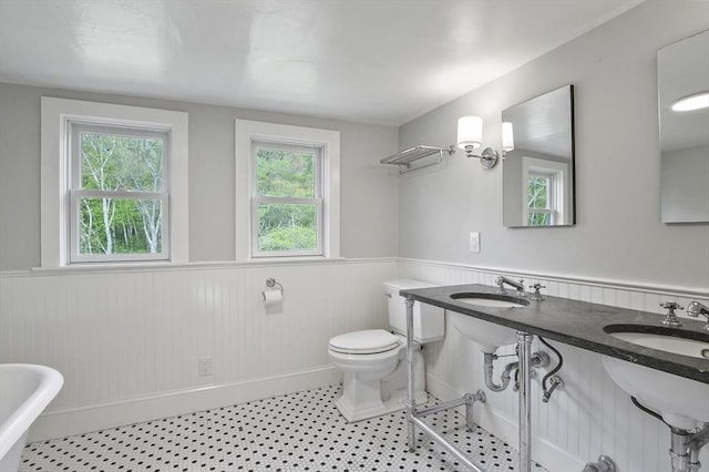 bathroom featuring a wainscoted wall, toilet, a freestanding tub, and baseboards