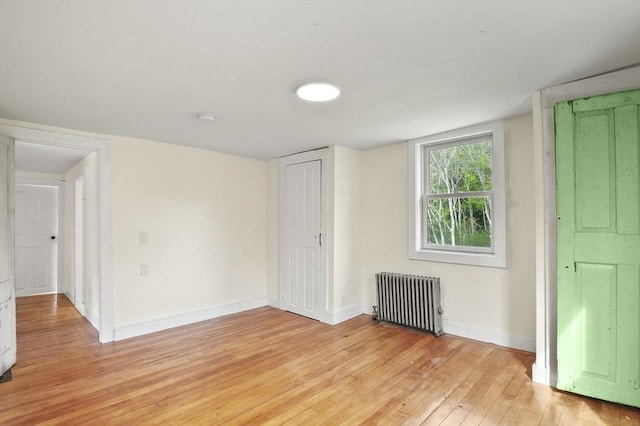 spare room with radiator, light wood finished floors, and baseboards