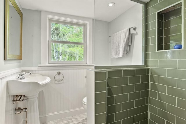 bathroom featuring wainscoting, a tile shower, and toilet