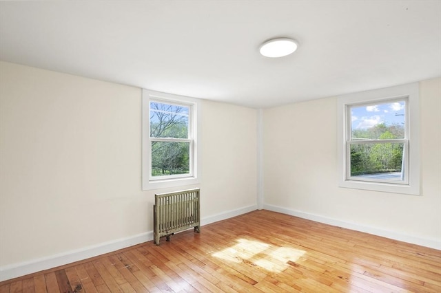 spare room featuring light wood finished floors, healthy amount of natural light, radiator, and baseboards