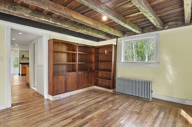 spare room featuring radiator heating unit, wood-type flooring, baseboards, healthy amount of natural light, and beamed ceiling