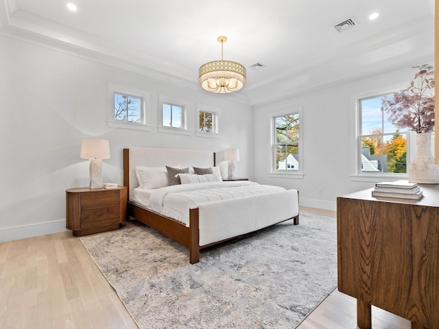 bedroom featuring ornamental molding, light hardwood / wood-style flooring, and a raised ceiling