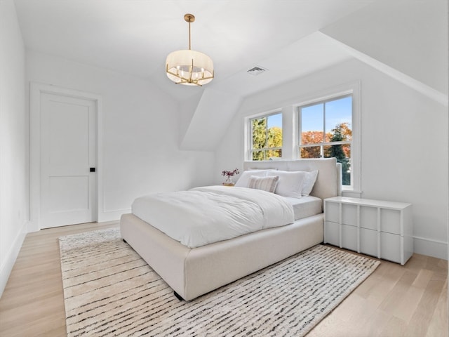 bedroom featuring an inviting chandelier, lofted ceiling, and light wood-type flooring