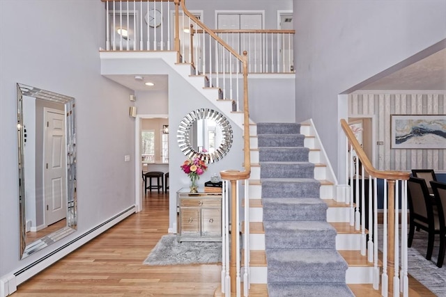 stairs featuring crown molding, a baseboard heating unit, hardwood / wood-style floors, and a towering ceiling