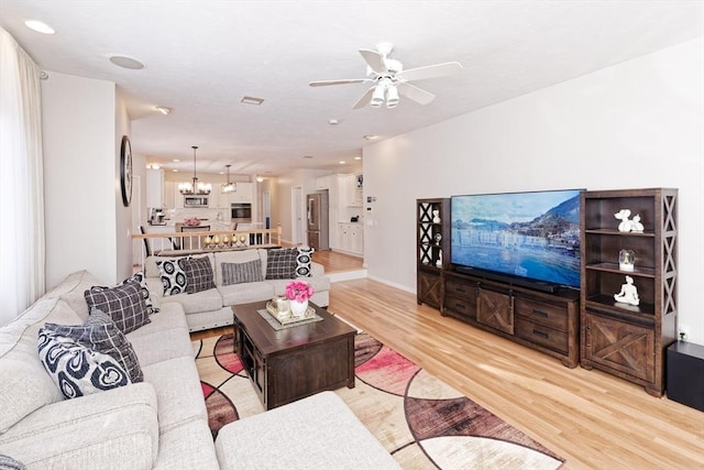 living room with ceiling fan with notable chandelier and light hardwood / wood-style floors