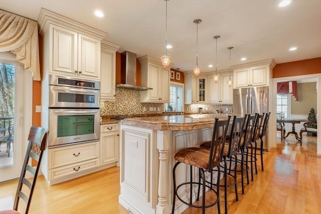 kitchen featuring decorative light fixtures, wall chimney exhaust hood, appliances with stainless steel finishes, plenty of natural light, and a kitchen island