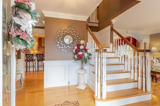 staircase featuring hardwood / wood-style floors, ornate columns, and ornamental molding