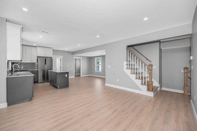 kitchen featuring stainless steel refrigerator, white cabinetry, light stone countertops, a kitchen island, and light wood-type flooring