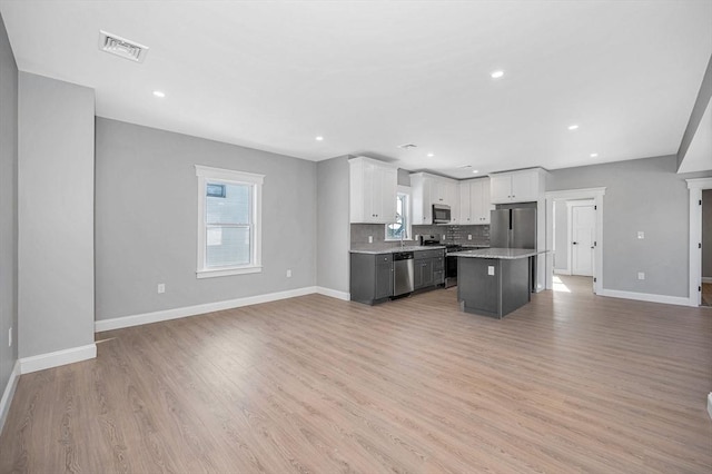 kitchen featuring appliances with stainless steel finishes, white cabinetry, tasteful backsplash, a healthy amount of sunlight, and a kitchen island