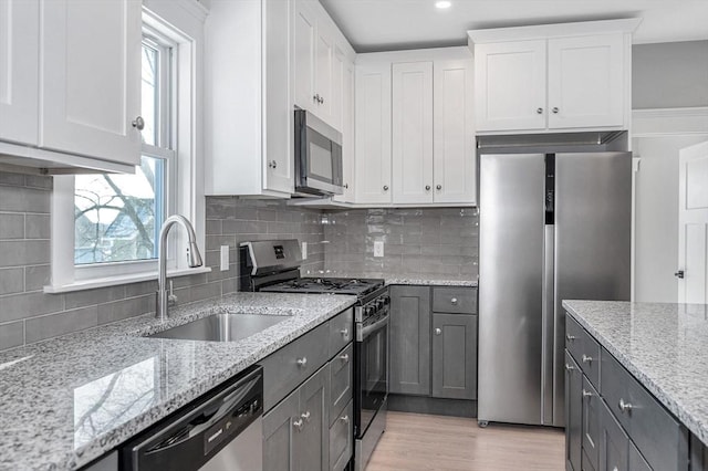 kitchen featuring sink, white cabinetry, light stone counters, appliances with stainless steel finishes, and decorative backsplash