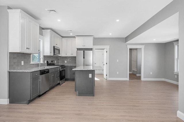 kitchen with appliances with stainless steel finishes, light stone countertops, a kitchen island, and white cabinets