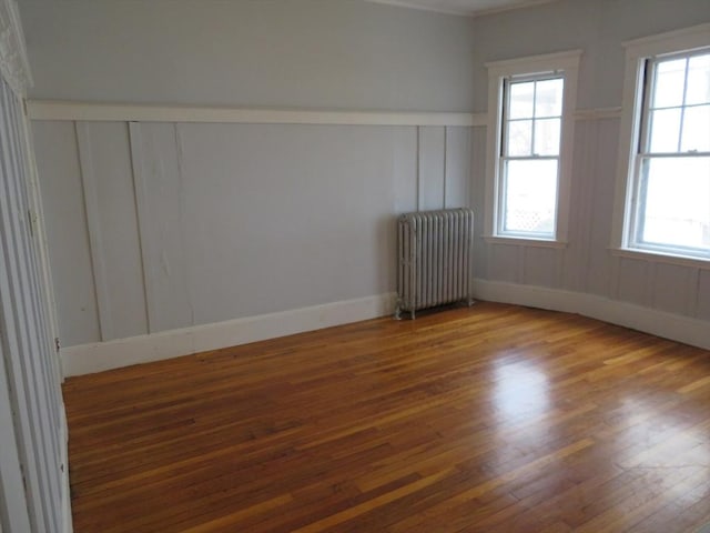 spare room with a decorative wall, radiator heating unit, and wood finished floors