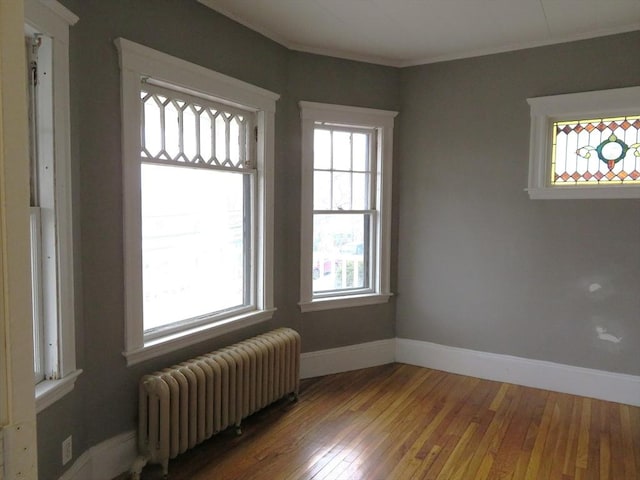 spare room with radiator heating unit, baseboards, wood-type flooring, and ornamental molding