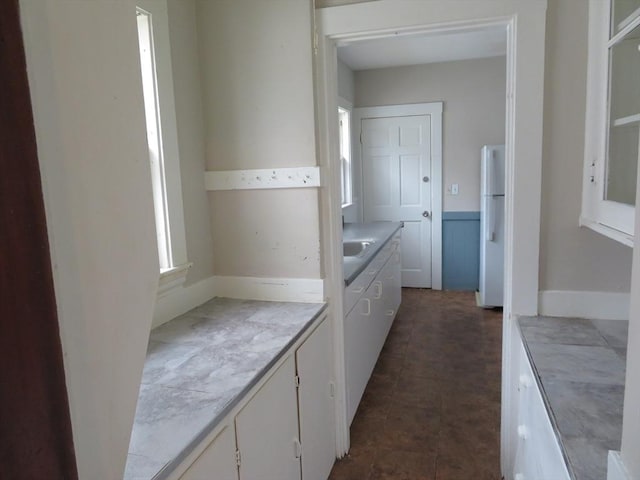 kitchen with light countertops, a sink, freestanding refrigerator, and white cabinetry