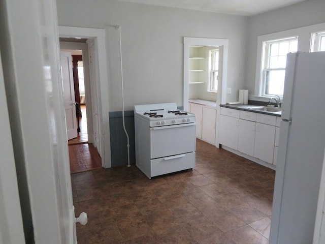 kitchen with white appliances, dark countertops, a sink, and white cabinets