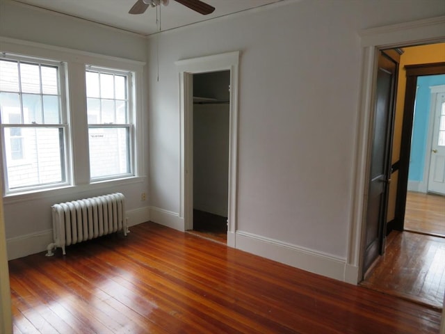 unfurnished bedroom featuring a closet, radiator, wood-type flooring, a ceiling fan, and baseboards